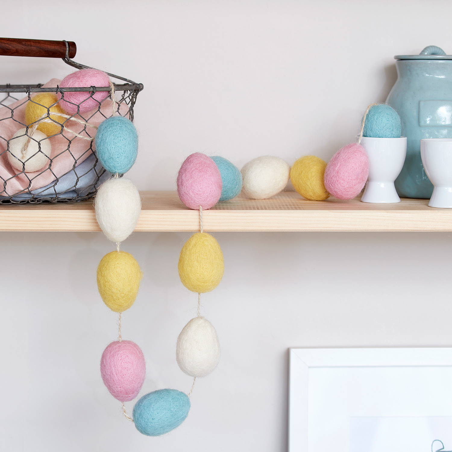 A blue, pink, yellow and cream egg cotton garland hanging on a kitchen shelf.