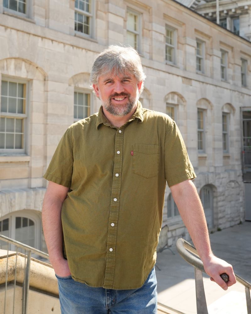 Smiling man in a green shirt standing near a building.