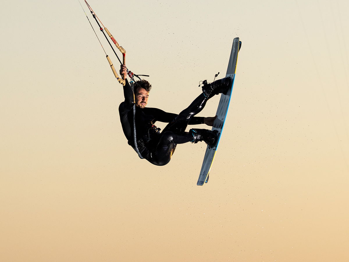 Person kitesurfing against a sunset background.