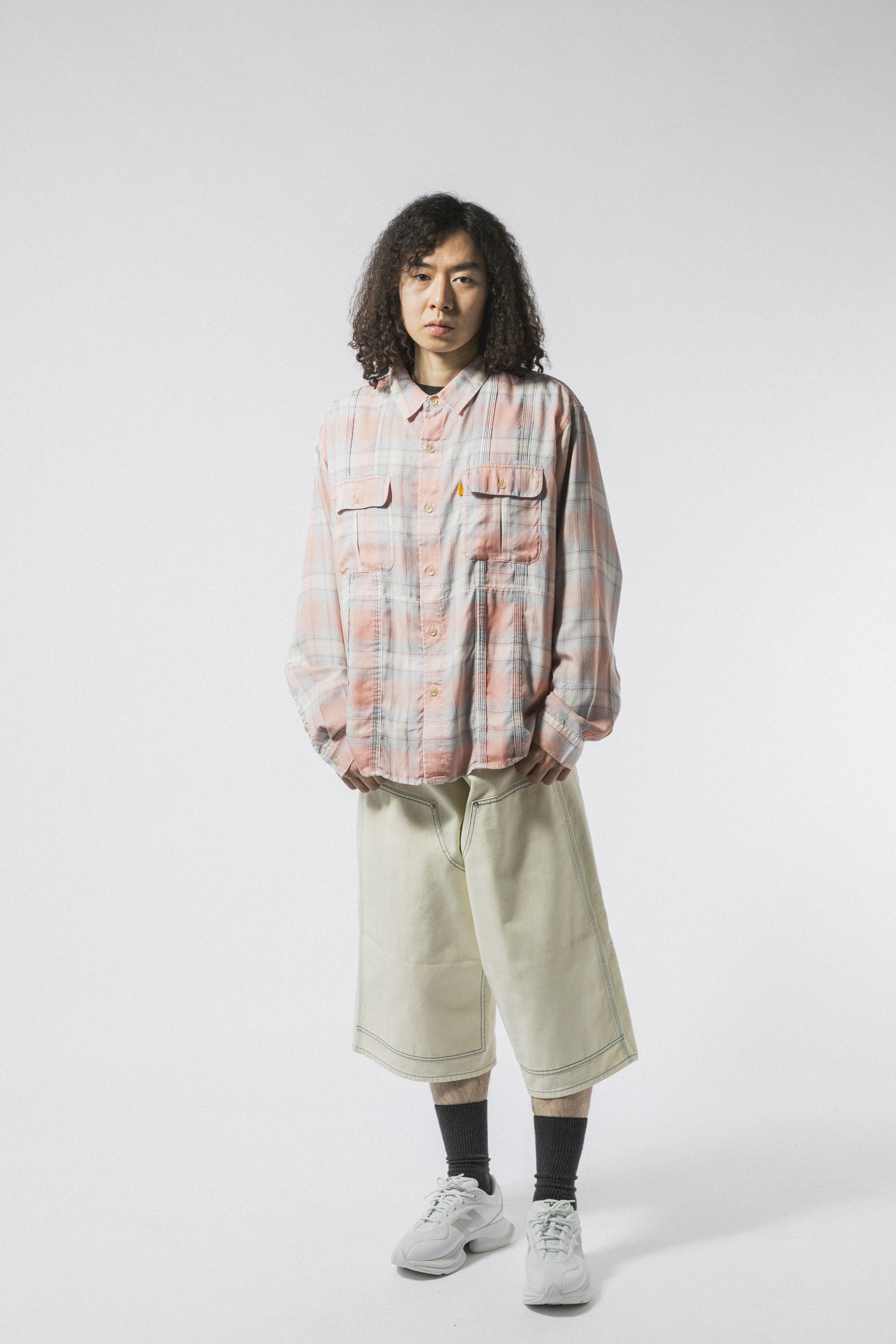Person wearing a plaid shirt and shorts, standing against a plain background.