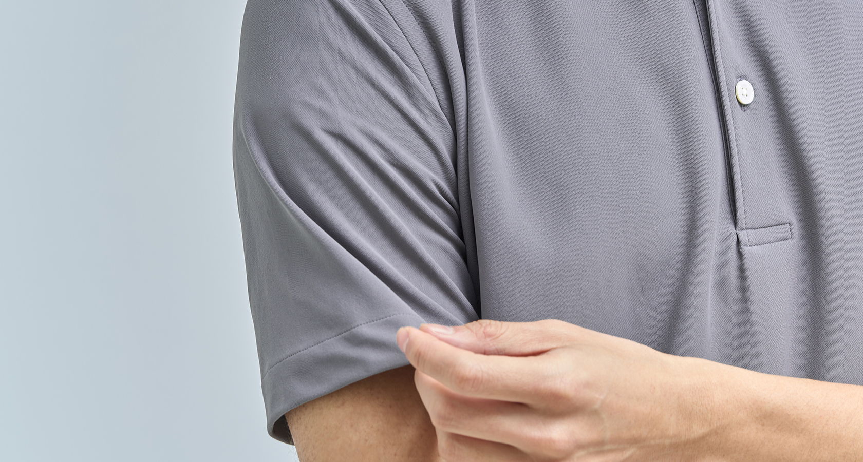 Person adjusting the sleeve of a gray polo shirt.