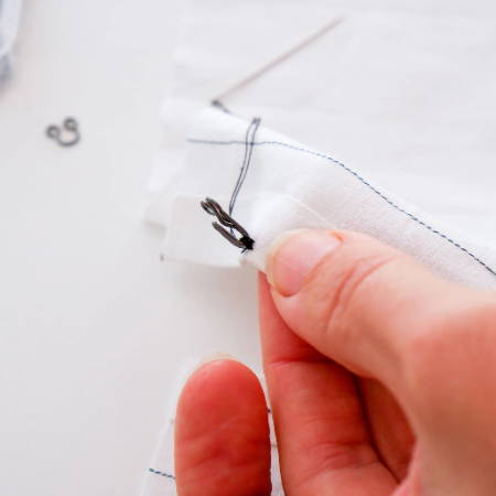 Detail of a hook from a hook and eye closure attached to a white fabric