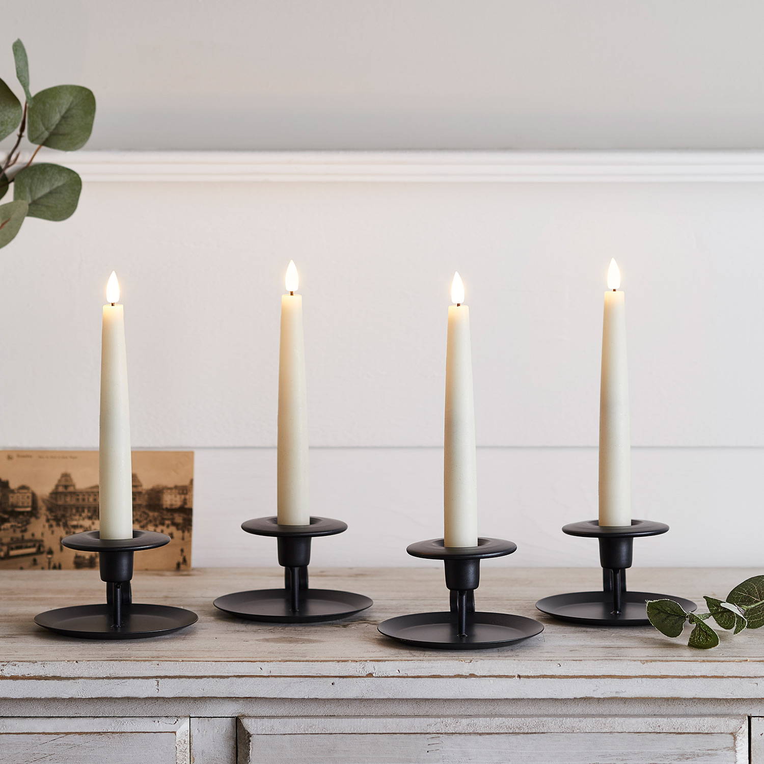 Short ivory taper candles in black candle holders illuminated on side table