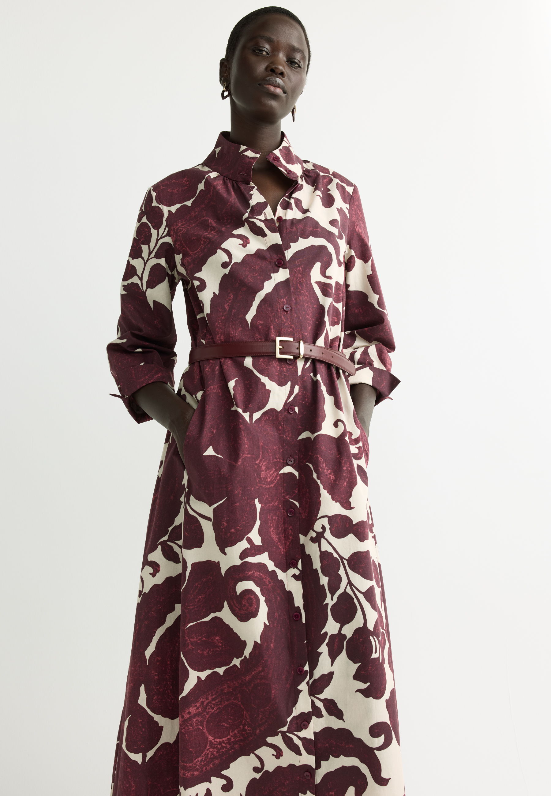 Model wearing a burgundy and white patterned dress with a belt.