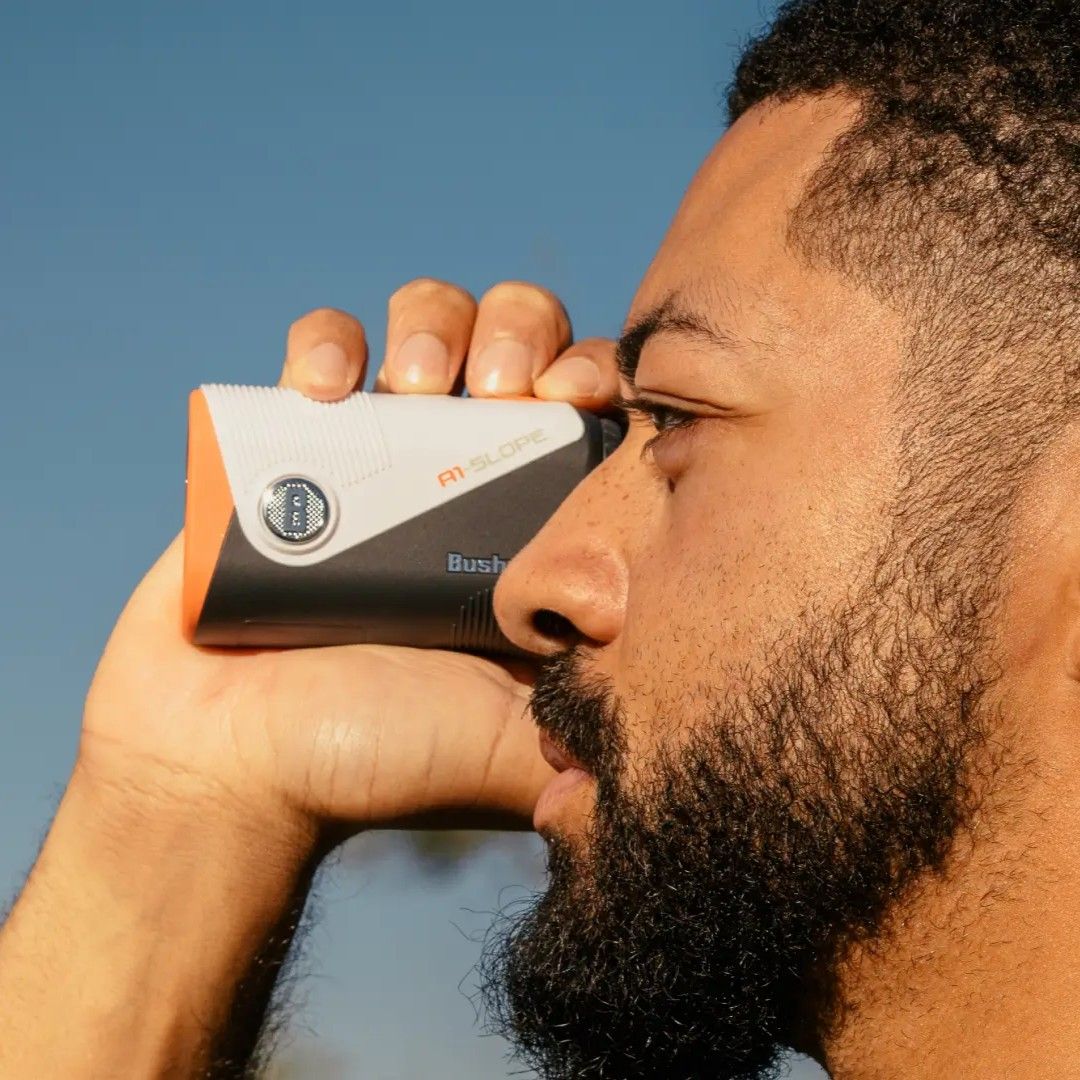 Man holding a device against his forehead, with a clear blue sky background.