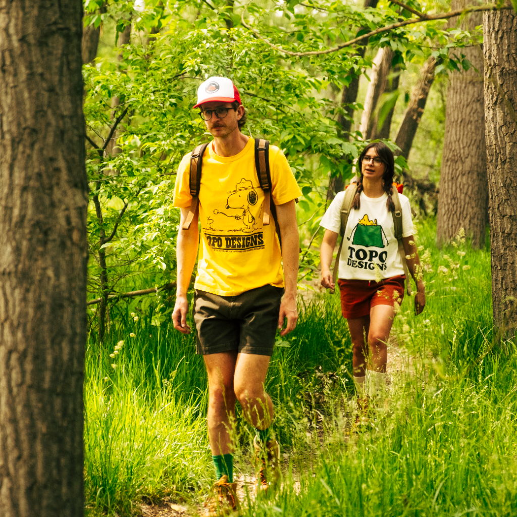 Two hikers walking on a trail surrounded by greenery.