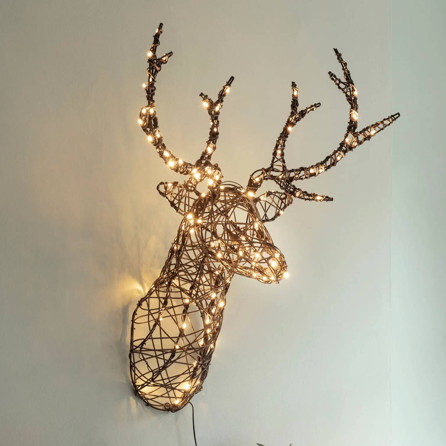 A rattan light up stag head hung on a green wall display 