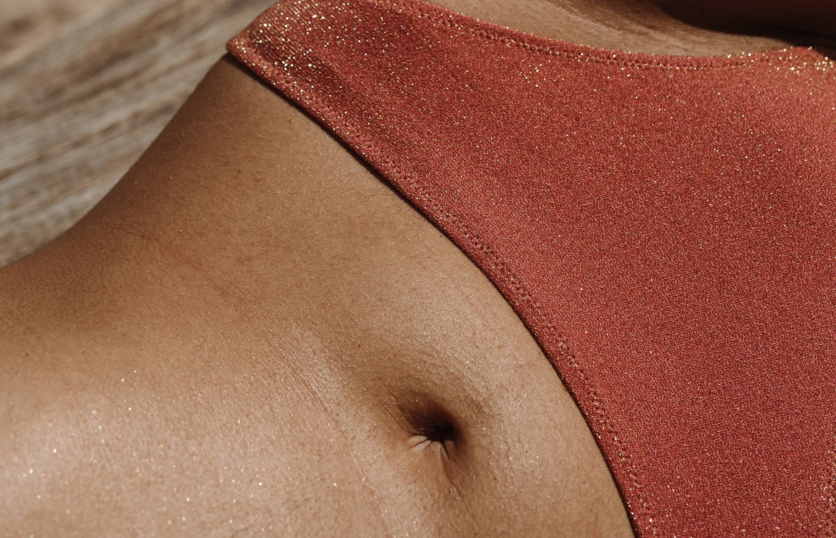 Close up of a woman’s belly button and pelvis dressed in shiny red underwear.