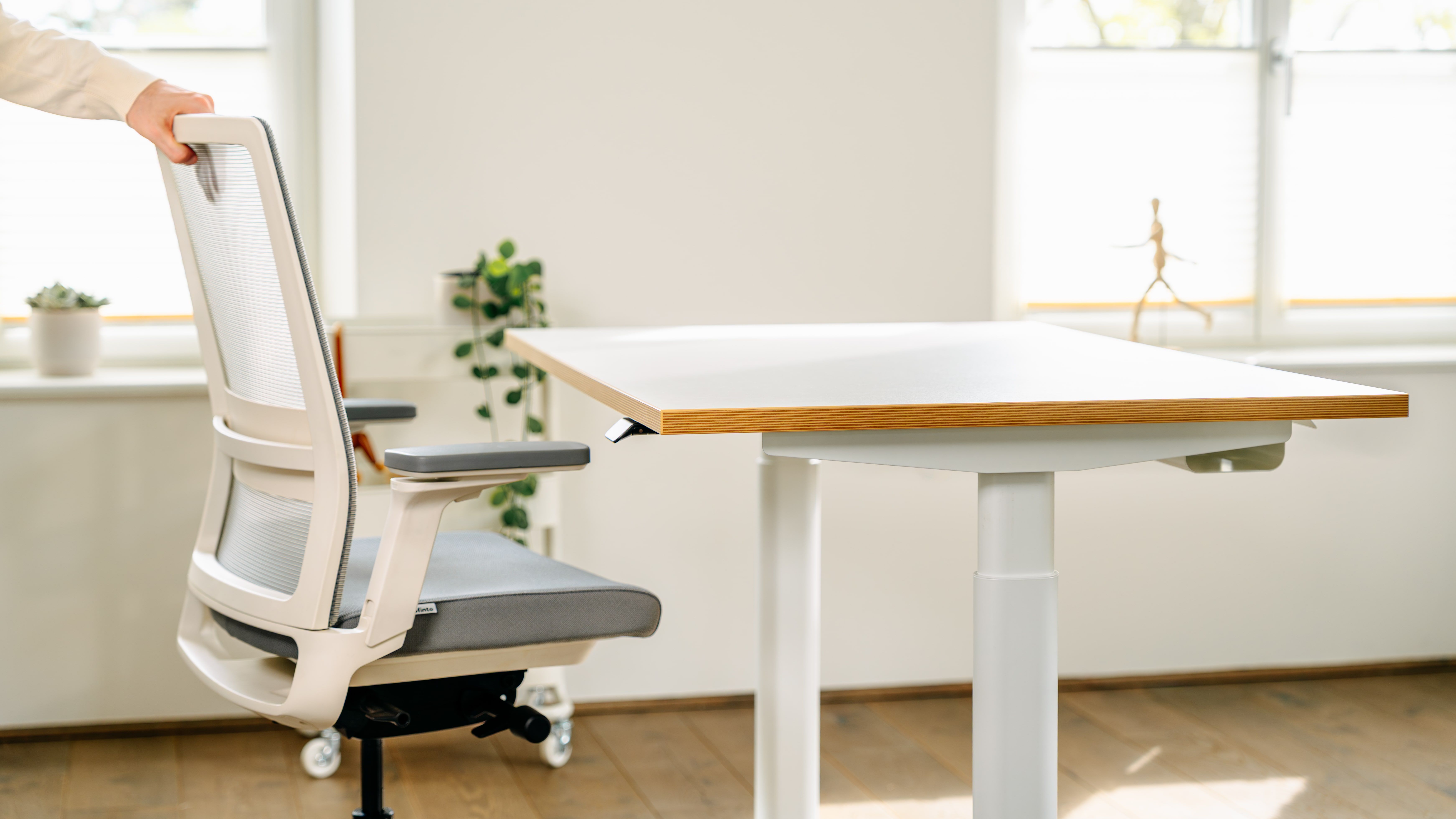 A person adjusting a modern office chair next to a desk.