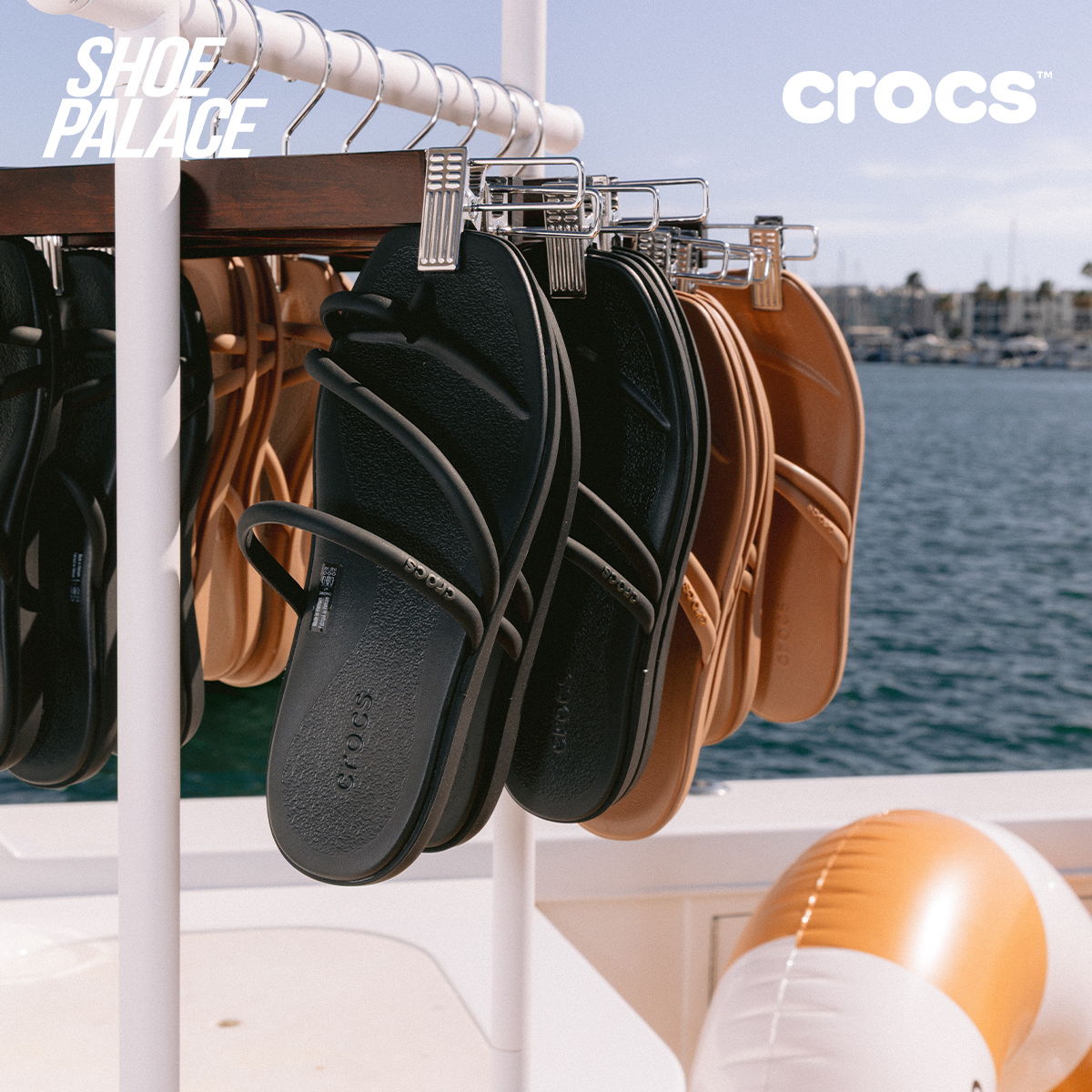 Hanging flip-flops by Crocs near water.