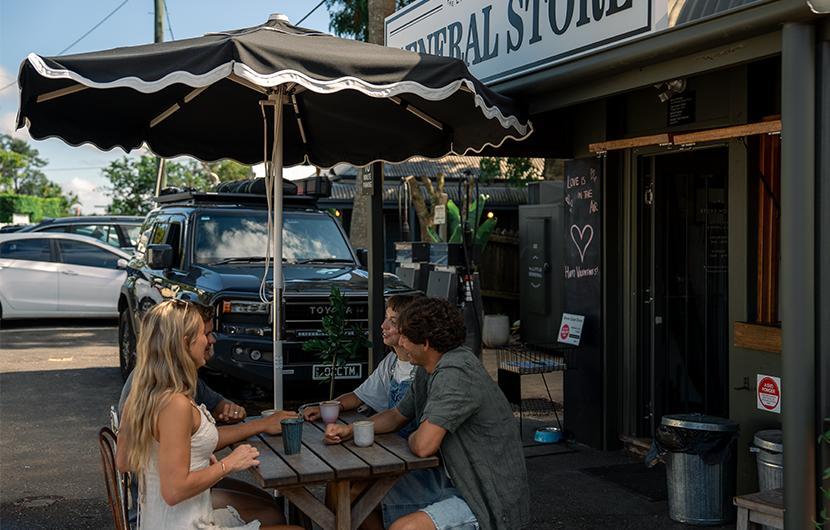 People having coffee in front of a general store with a loaded vehicle in the background