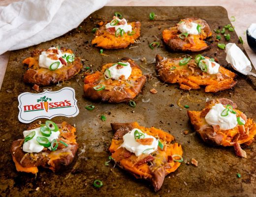 Baked sweet potatoes topped with sour cream and green onions on a baking sheet.