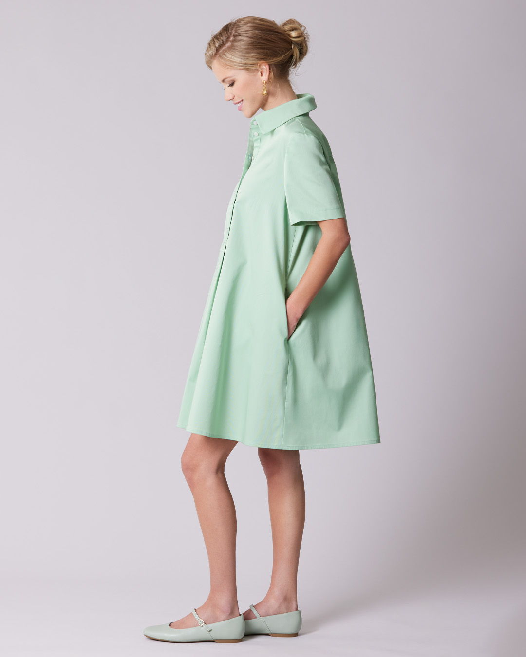 A woman in a mint green dress standing sideways with pockets.
