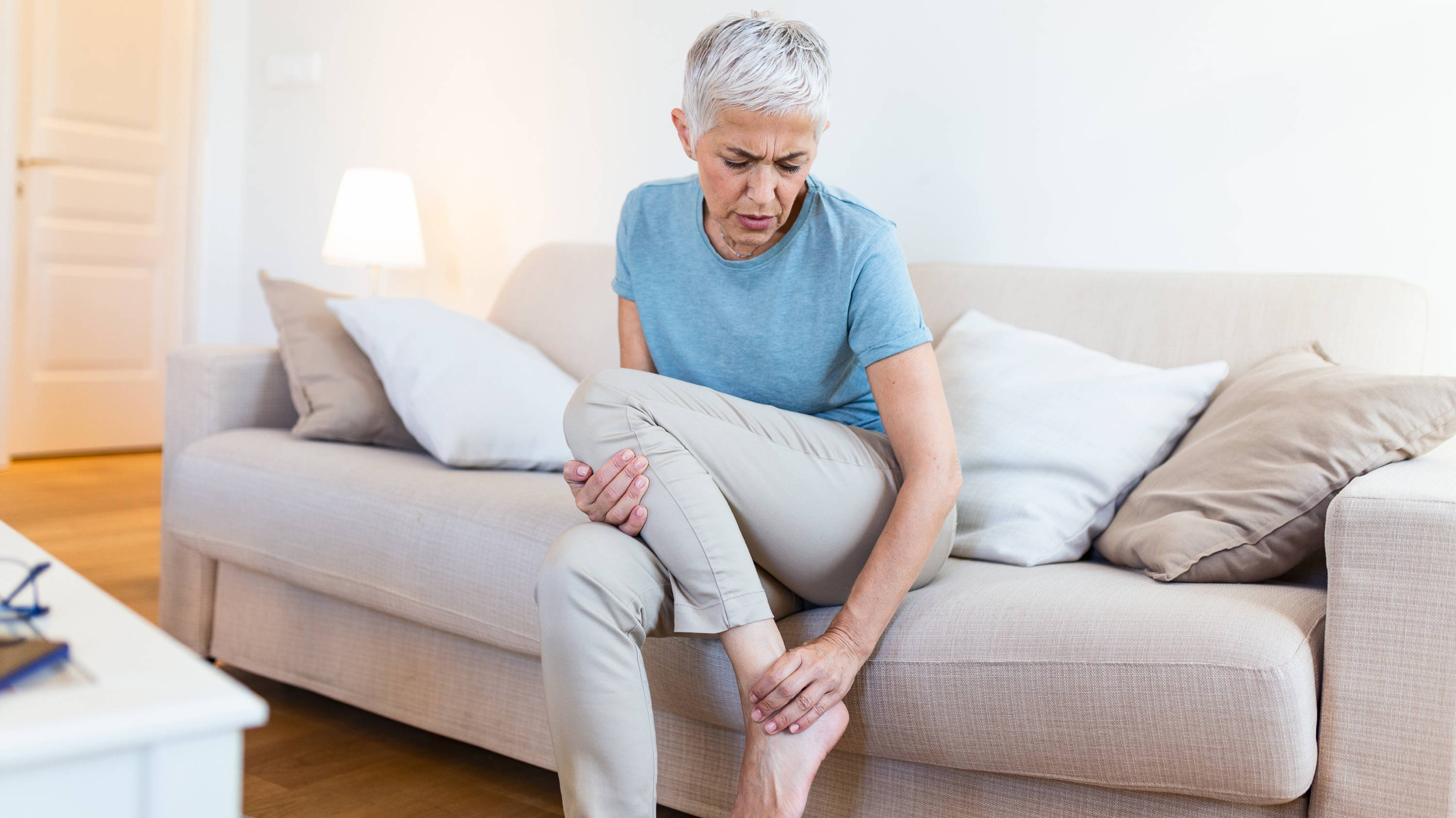 Older woman sitting on couch, massaging  a painful foot and leg