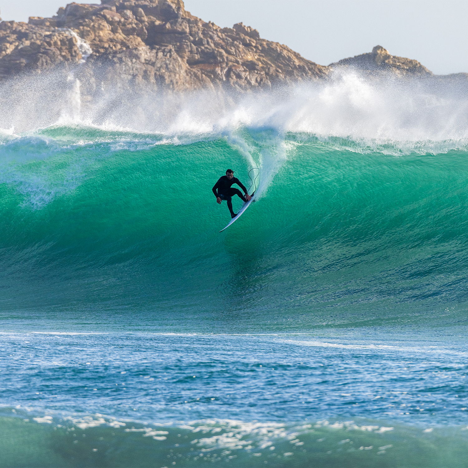Un surfeur qui surf une grande vague turquoise, avec des falaises rocheuses en arrière-plan_Duotone_Ion Water