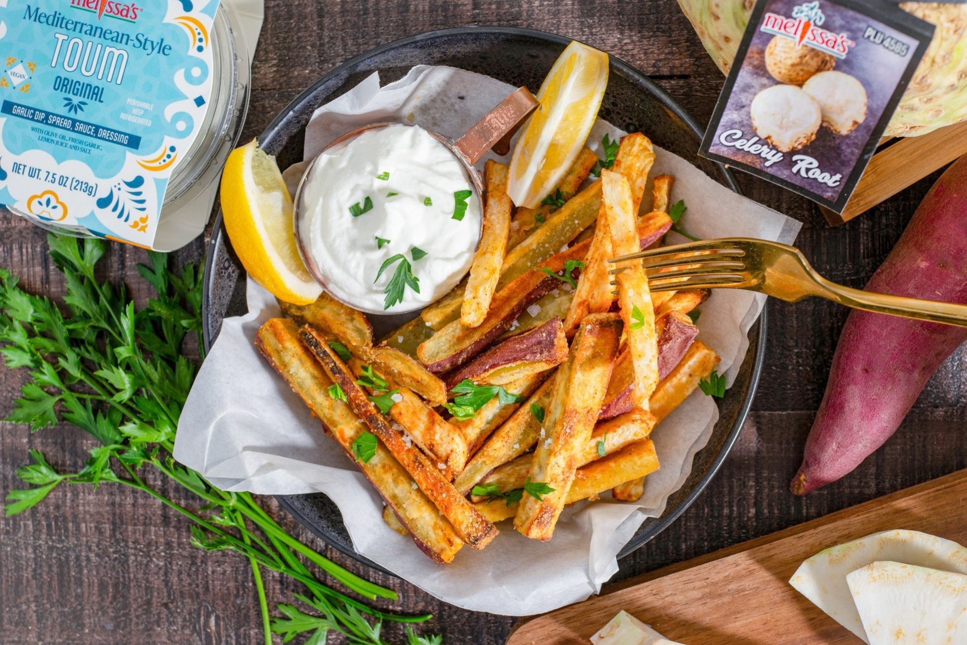Plate of fries with dip, lemon, and herbs on a wooden table.