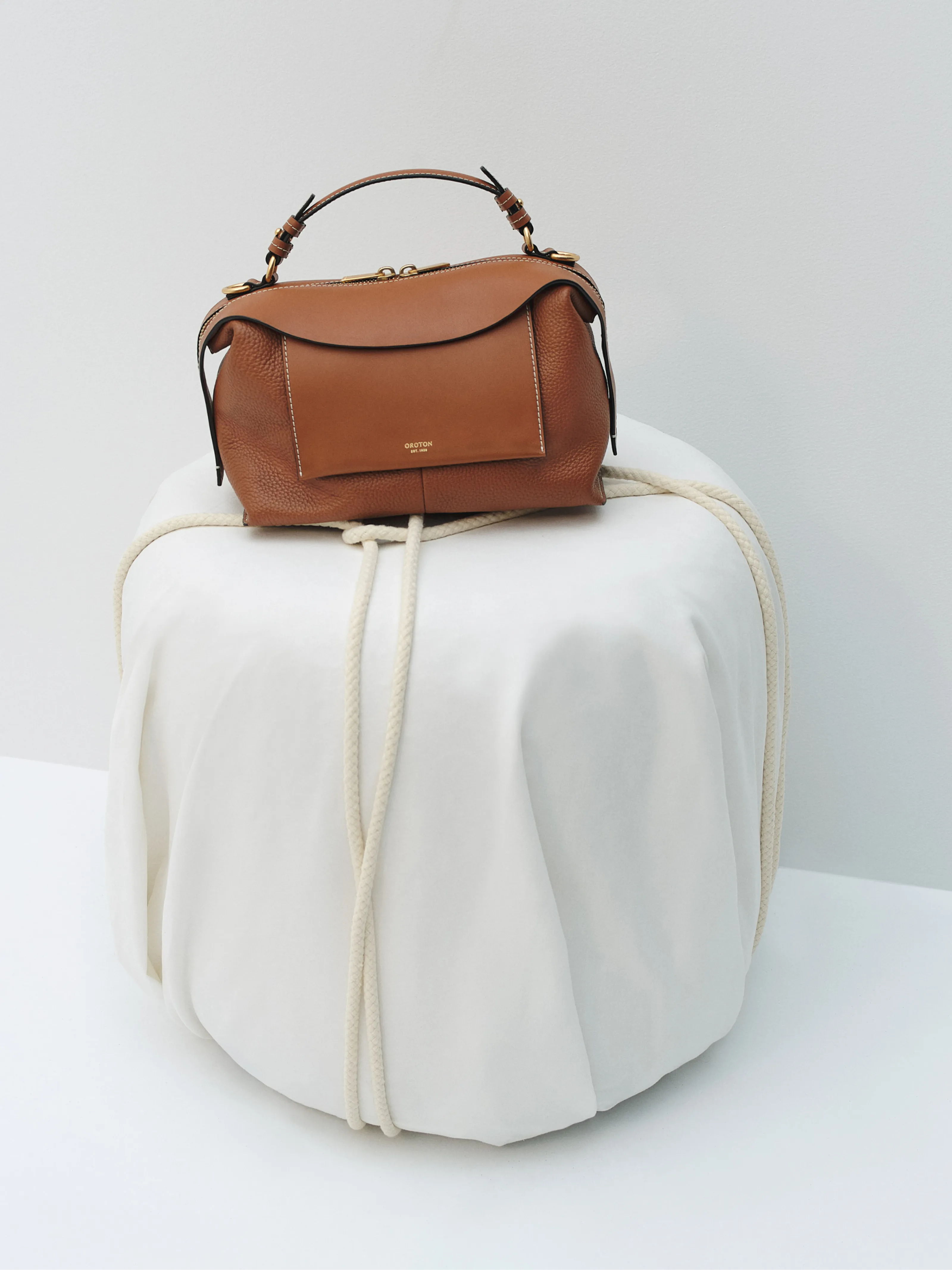 A brown handbag resting on a white circular pouf with rope details.