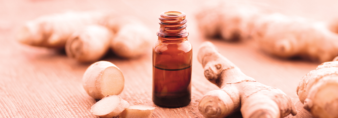Brown essential oil bottle surrounded by ginger root on a wooden surface.