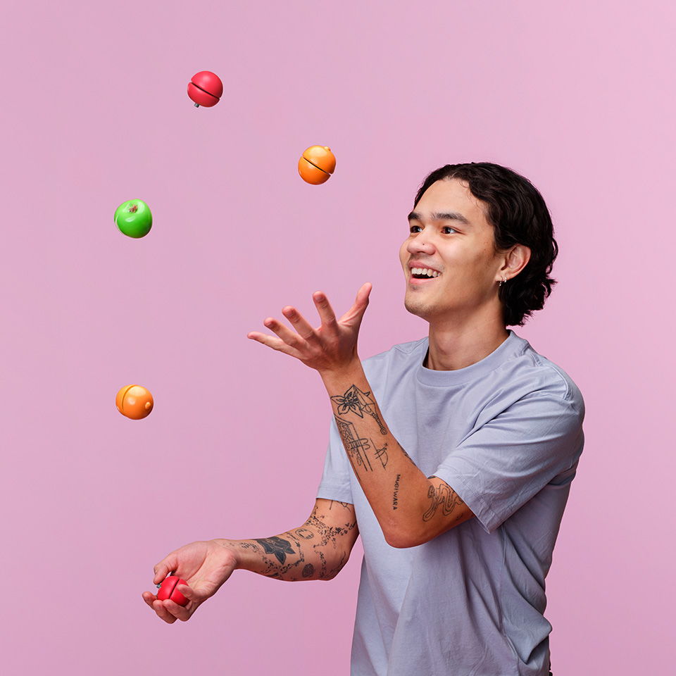 A person juggling colorful balls against a pink background.