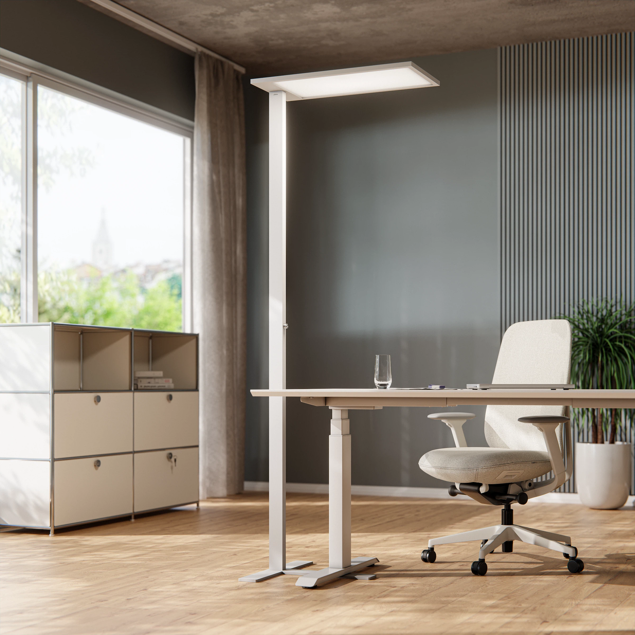 A white " Lumino " floor lamp next to a height-adjustable desk and office chair in a bright, modern office.