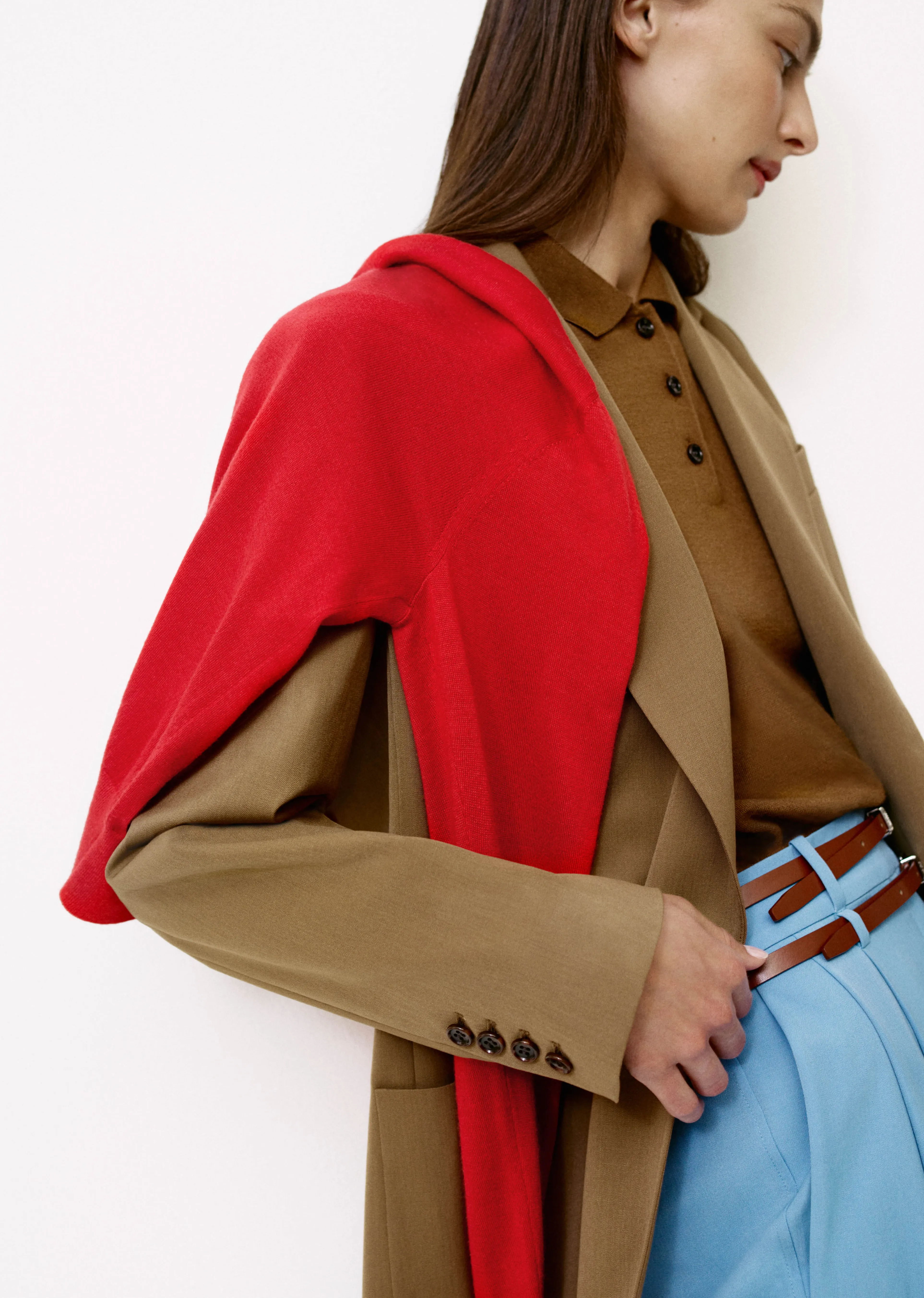Woman in a brown coat with a red shawl and blue pants.