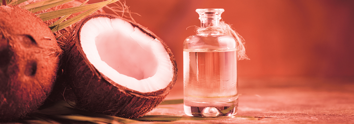 Coconut half beside a glass bottle of coconut oil on a wooden surface.