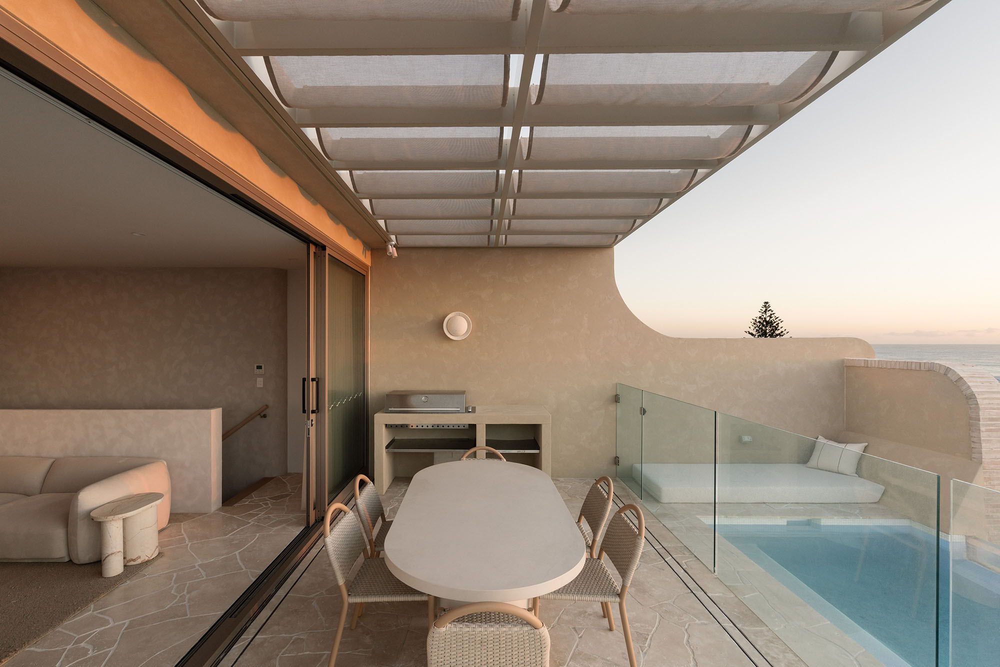 Modern balcony with table, chairs, the Fossil Coral Eclipse Wall Sconce, and pool overlooking a scenic view.