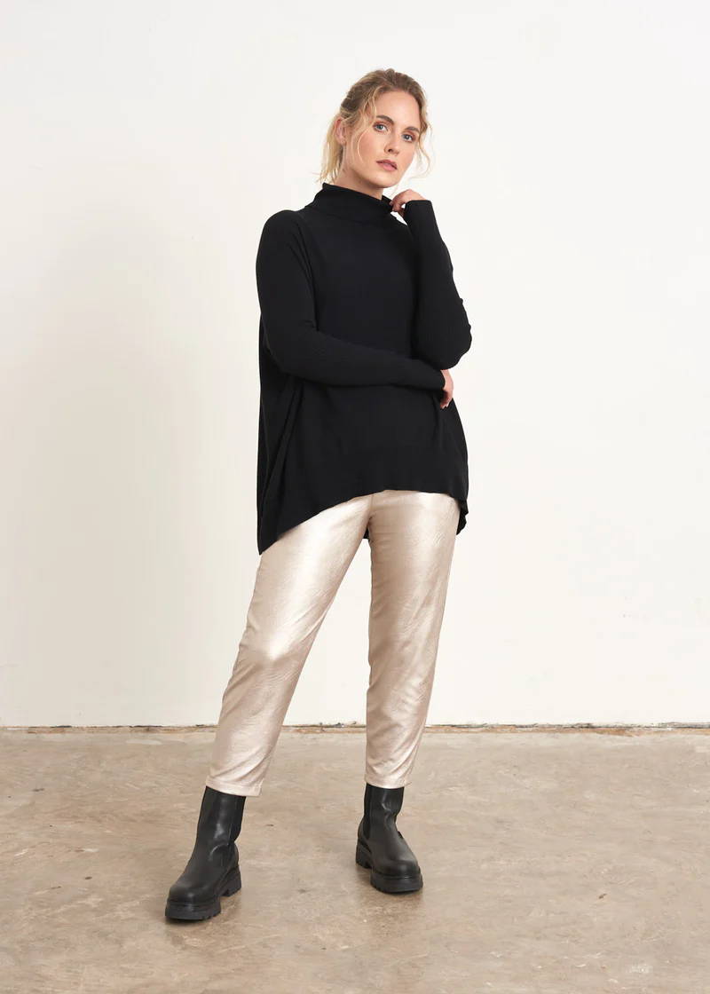 A model wearing a pair of champagne gold faux leather trousers with a black turtle neck sweater and black chunky leather chelsea boots