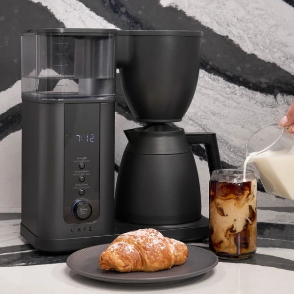 Coffee maker, grinder, croissant, and iced coffee with milk on a table.