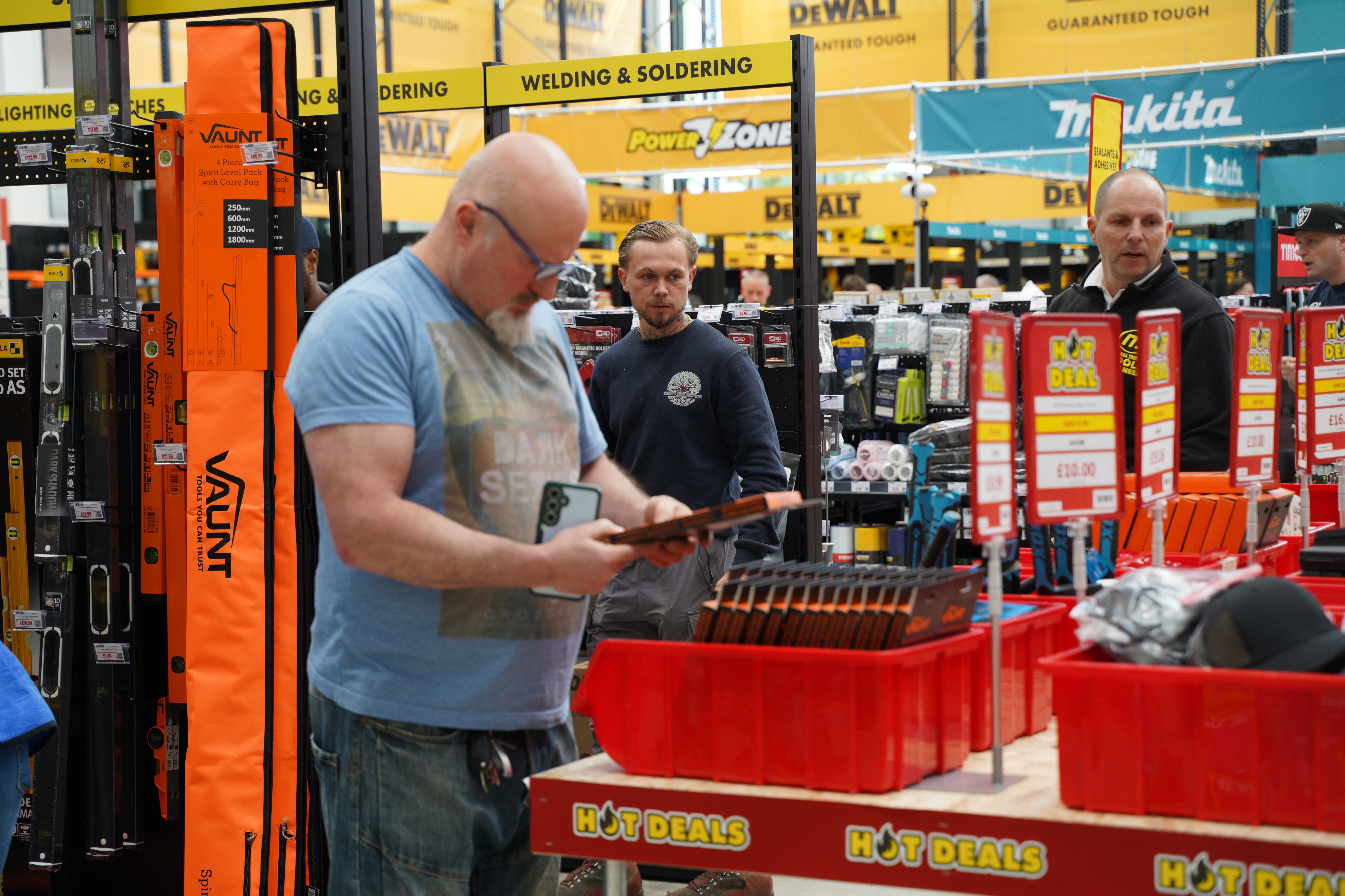 Man examining tools in a store aisle with other shoppers nearby.