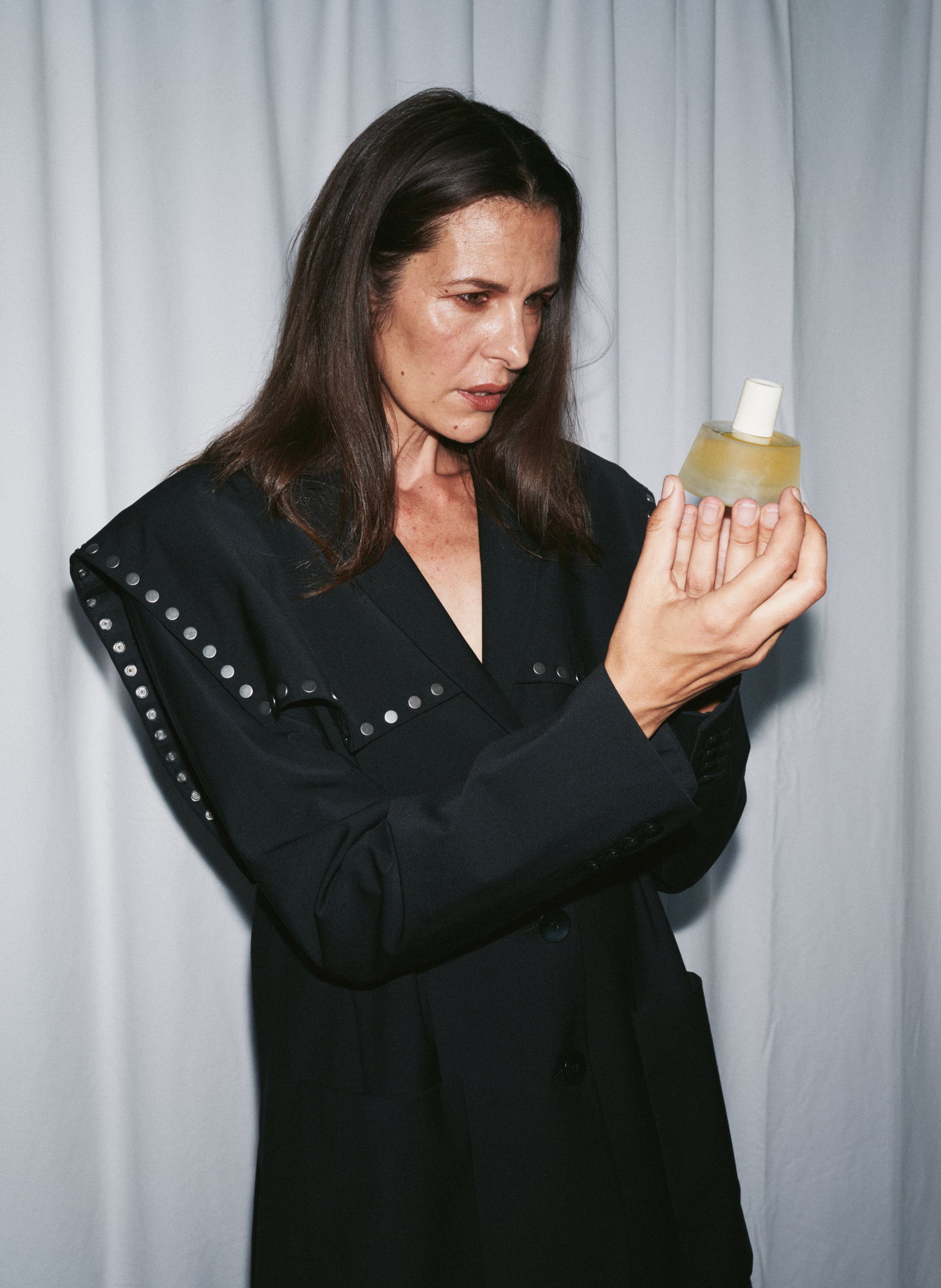 A woman in a black outfit holds a bottle, looking thoughtfully at it.