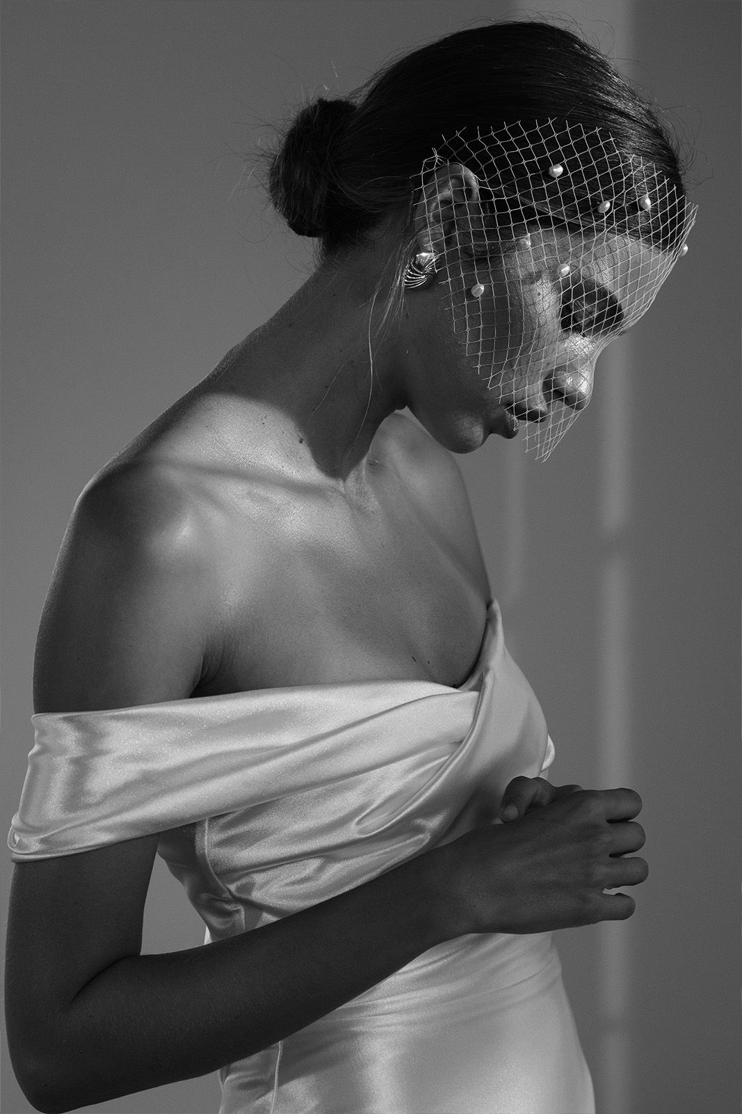 A woman in a satin dress with a netted veil, looking down thoughtfully.