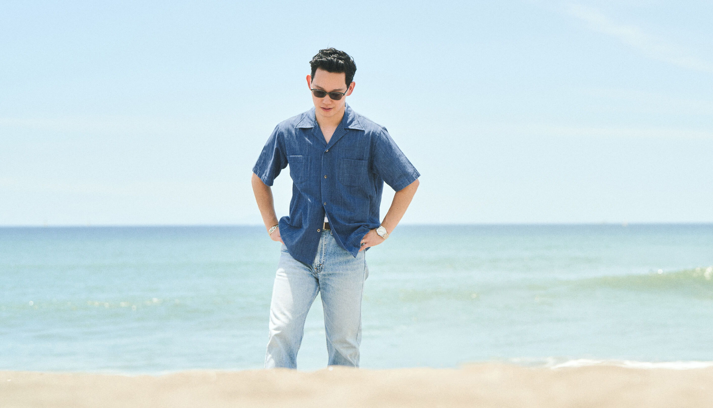 A person in sunglasses walking on the beach by the ocean.