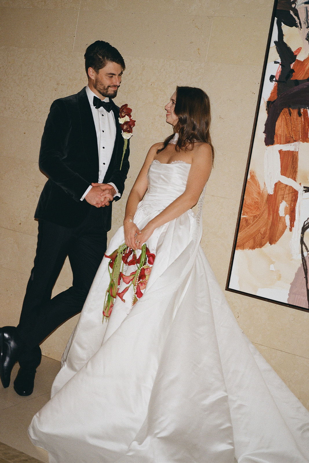 Bride and groom in formal attire, smiling, against an artistic background.
