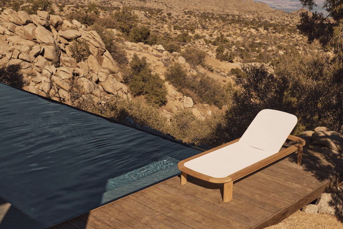 Modern pool lounge chair with white cushion beside a desert infinity pool, showing outdoor chaise furniture in a rocky Arizona landscape.
