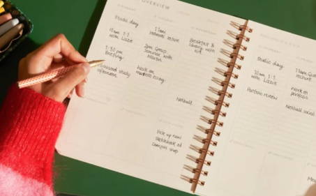 A woman's hand writing on a planner, organizing her schedule and tasks efficiently.