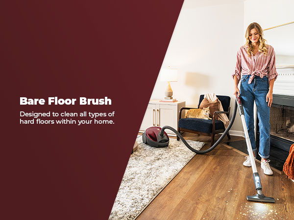 Woman using a vacuum with a bare floor brush in a living room.