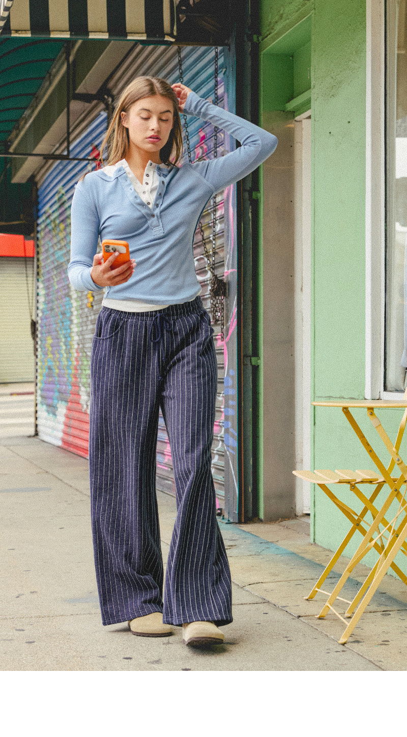 Woman walking in striped pants and a blue top, holding an orange.