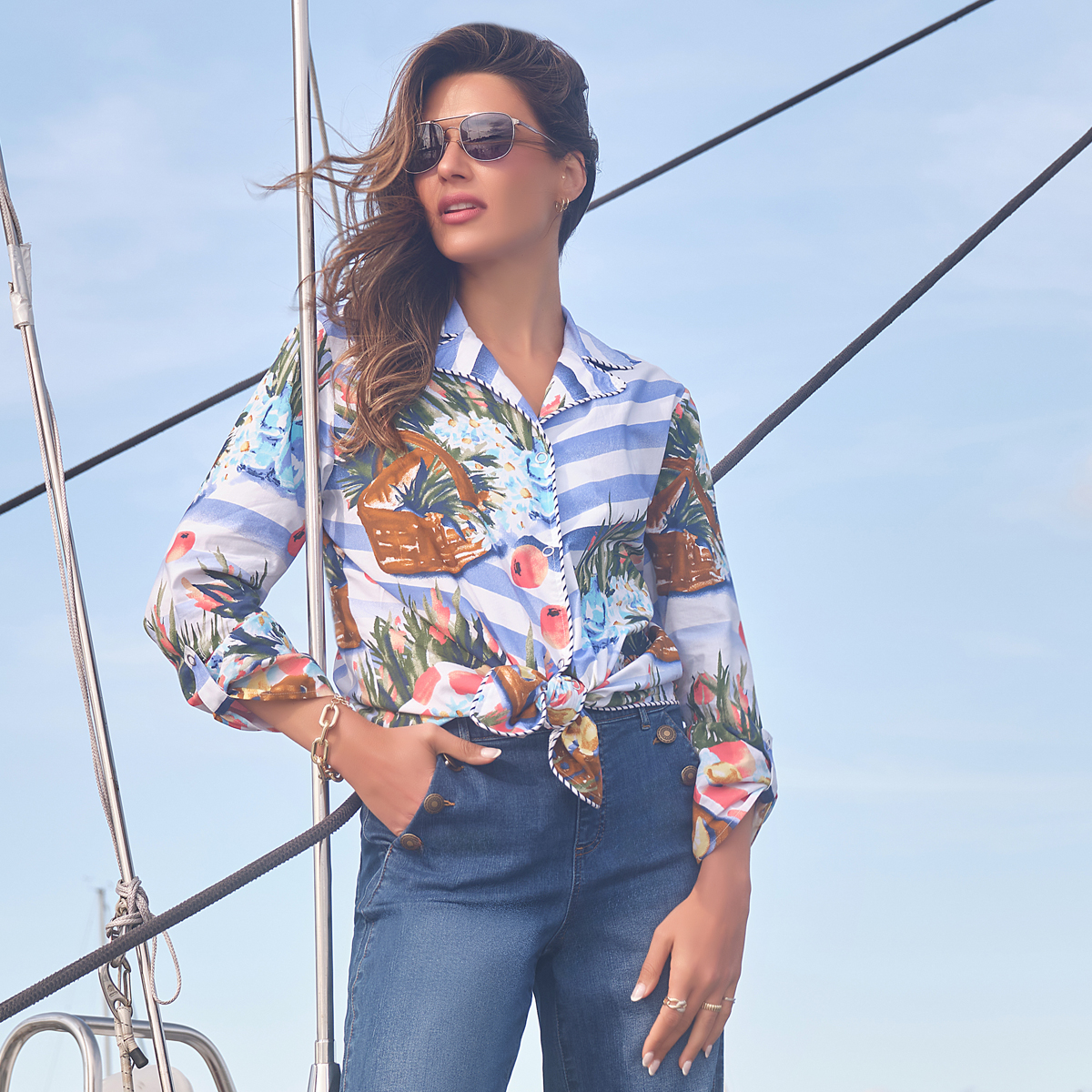 Woman in a colorful shirt and sunglasses on a sailboat.
