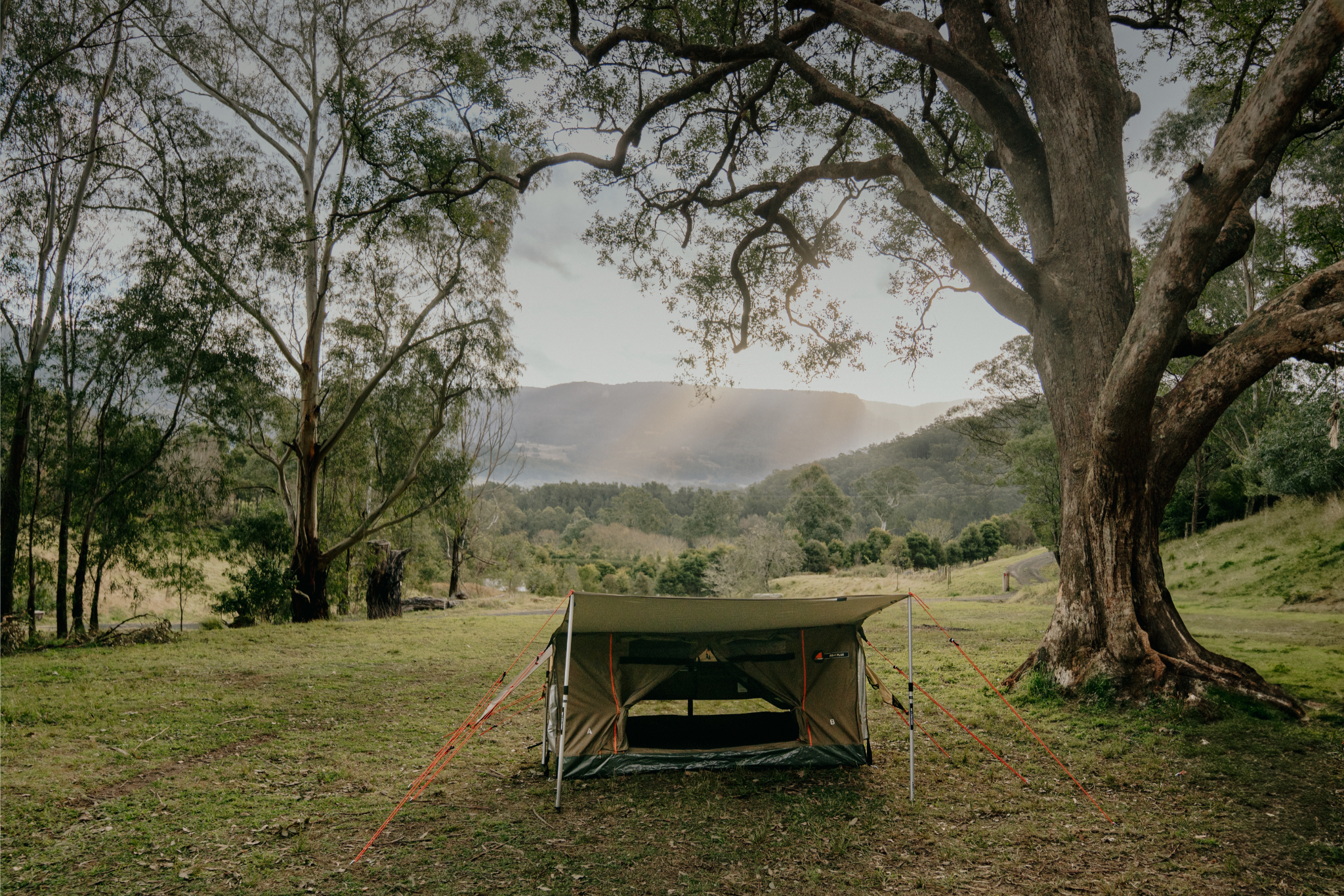 A tent set up in a grassy area surrounded by trees and hills.