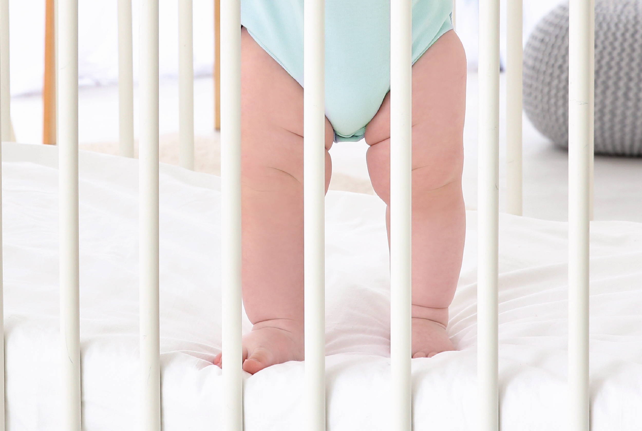 Baby standing on edge of crib mattress with edge support for safety.
