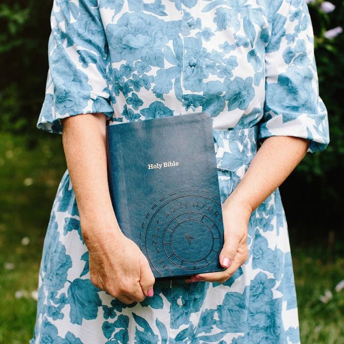 Woman in a blue floral dress holding a book outdoors.
