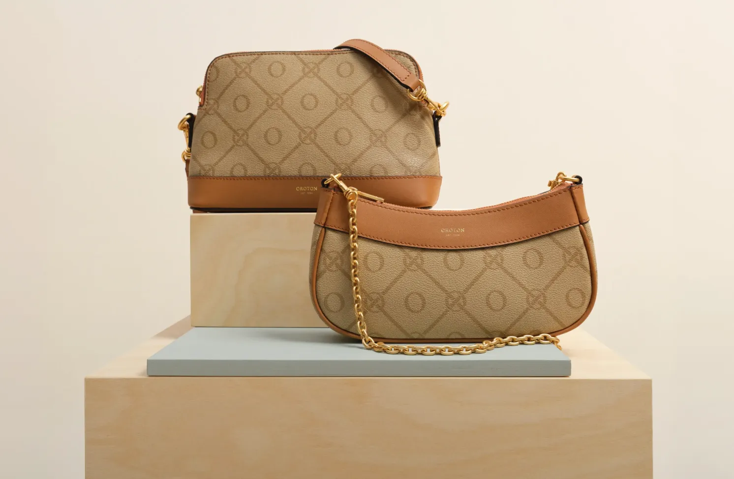 Two stylish handbags displayed on a wooden pedestal against a neutral background.