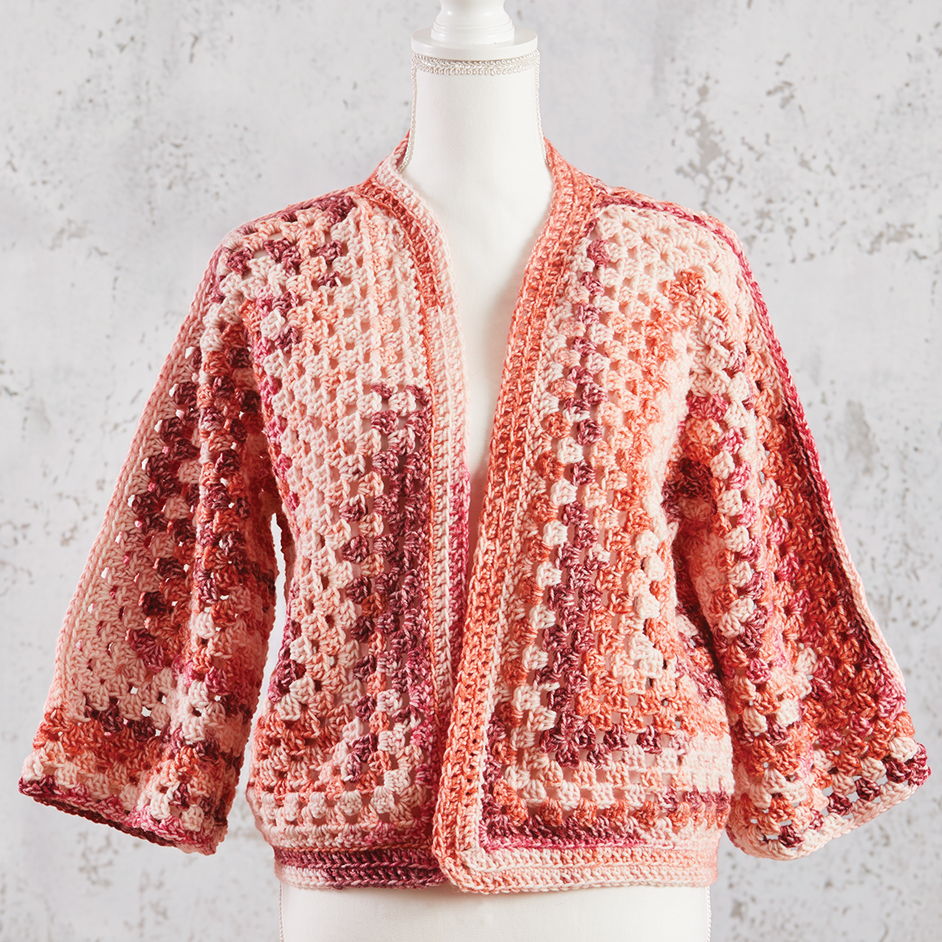 Crocheted cardigan in shades of pink & coral displayed on a mannequin.