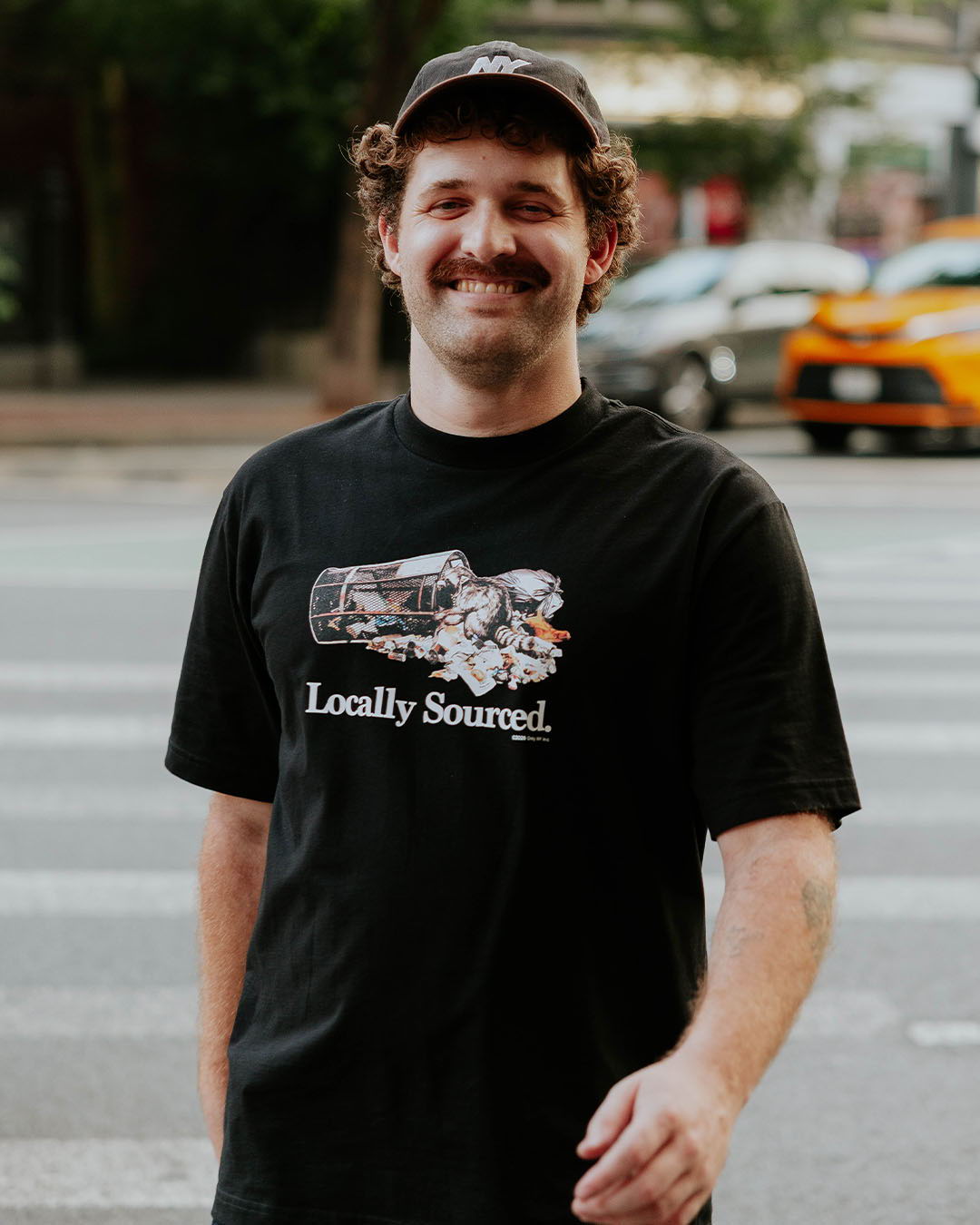 Smiling man in a black shirt standing on a city street.
