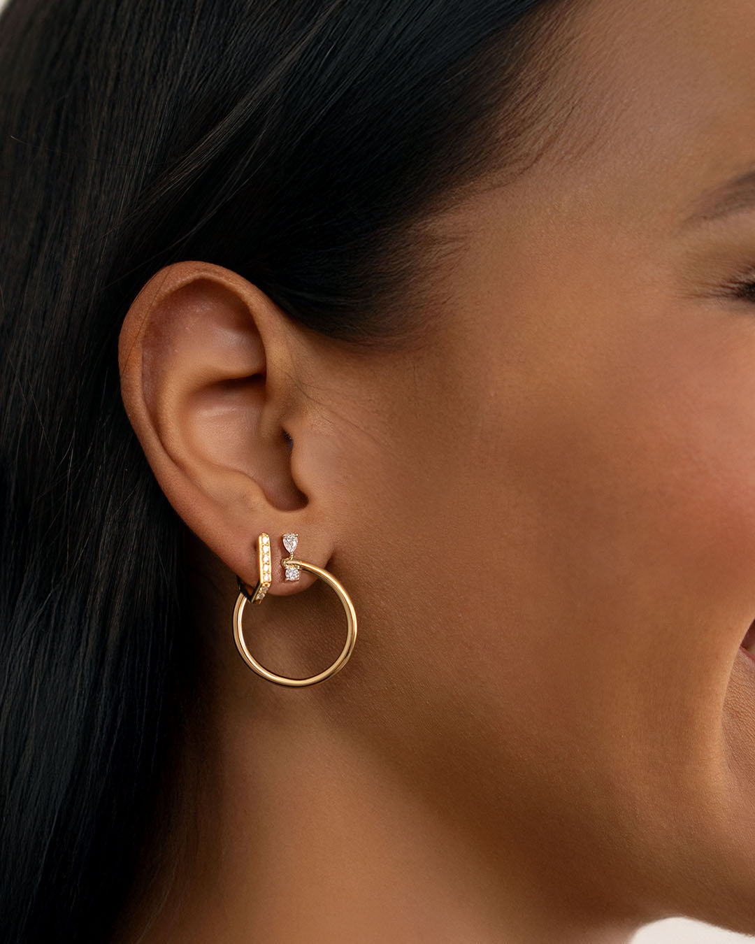 Close-up of a person wearing hoop earrings with a gold design.