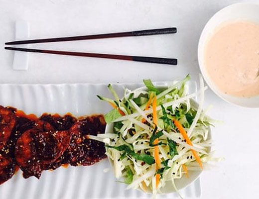 Grilled meat with salad and dipping sauce, served with chopsticks.