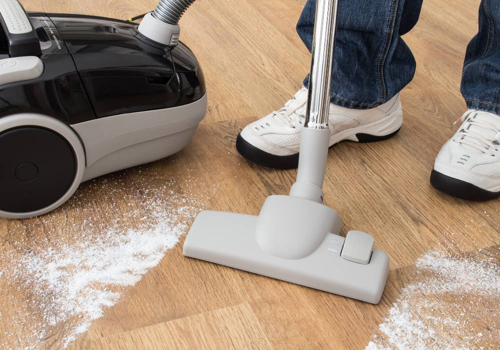 Person vacuuming up white powder from hardwood floors