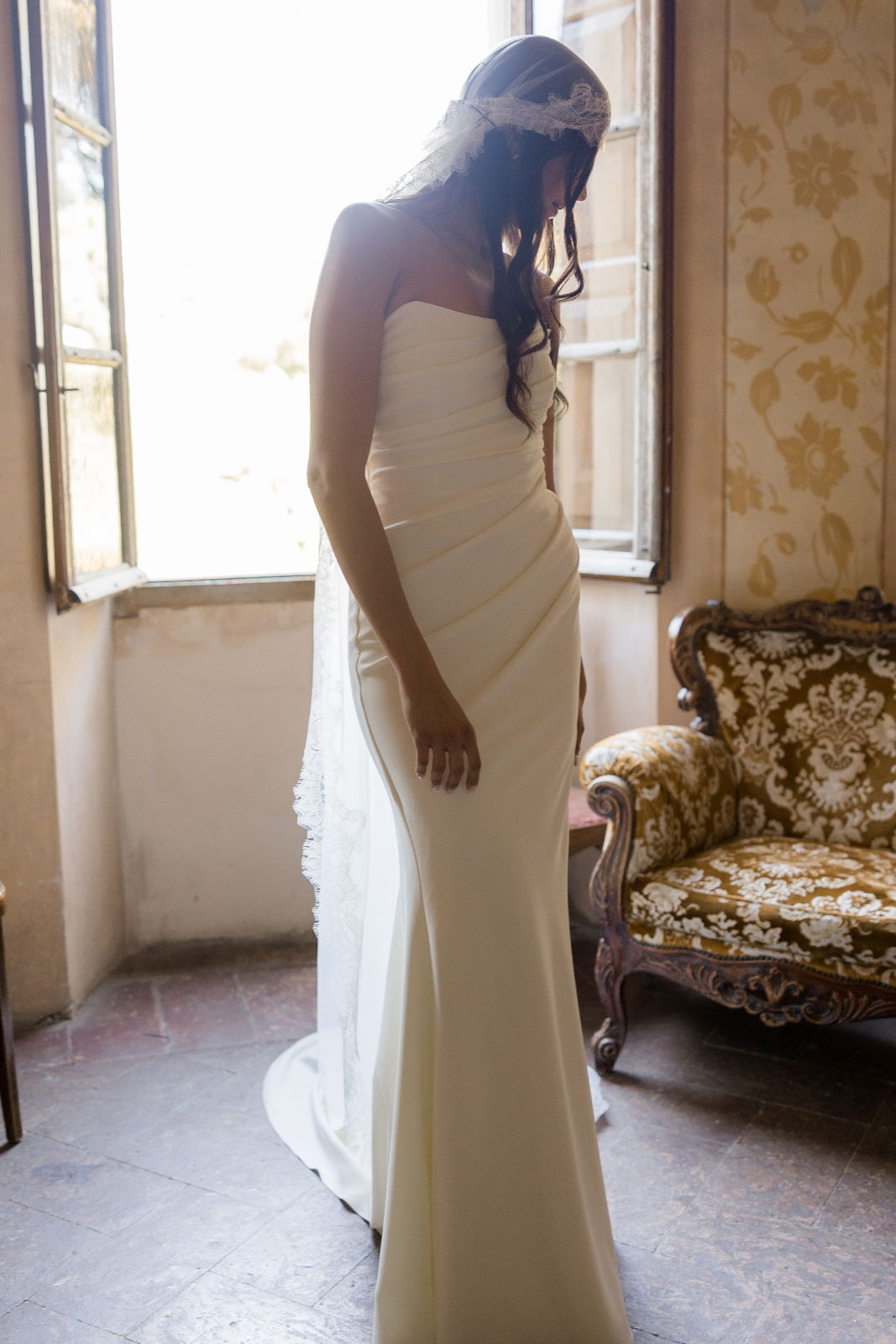 Bride in a white wedding dress standing by a window.