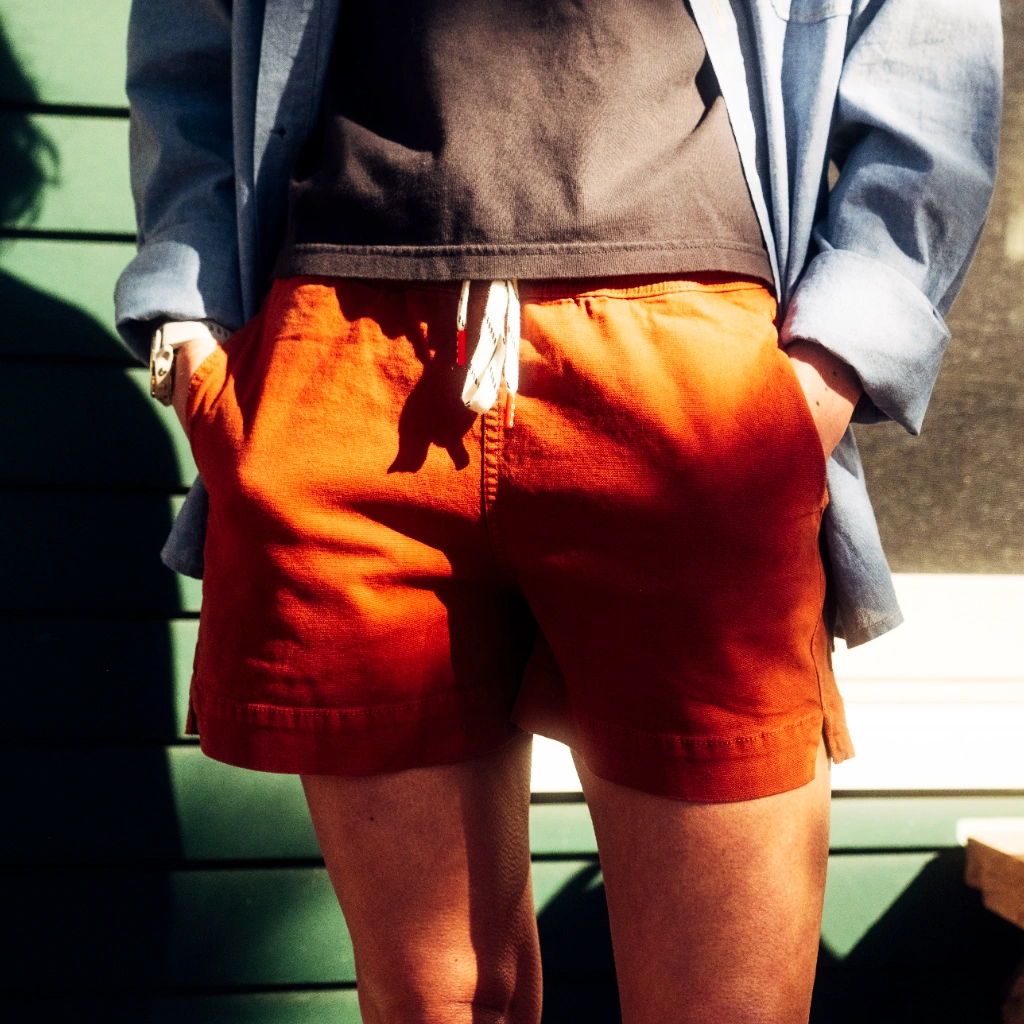 Person wearing orange shorts and a dark shirt, hands in pockets.
